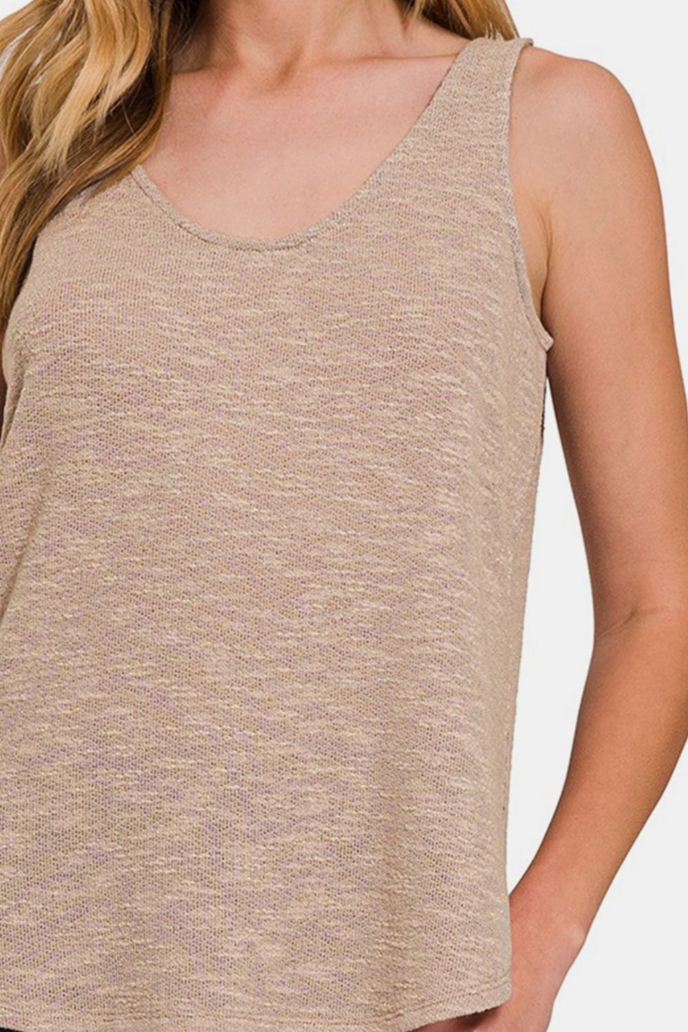 A woman with long, blonde hair wears a Zenana Curved Hem Round Neck Tank in beige and blue jeans, perfect for a casual wardrobe, standing against a plain background.