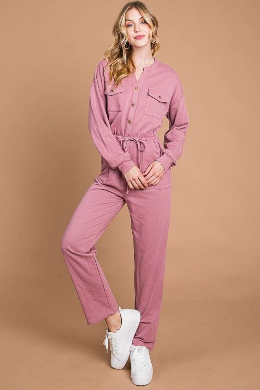 Against a beige background, an individual models the Culture Code Full Size Button Up Drawstring Waist Straight Jumpsuit, which features a stylish pink design with pockets and a chic drawstring waist.