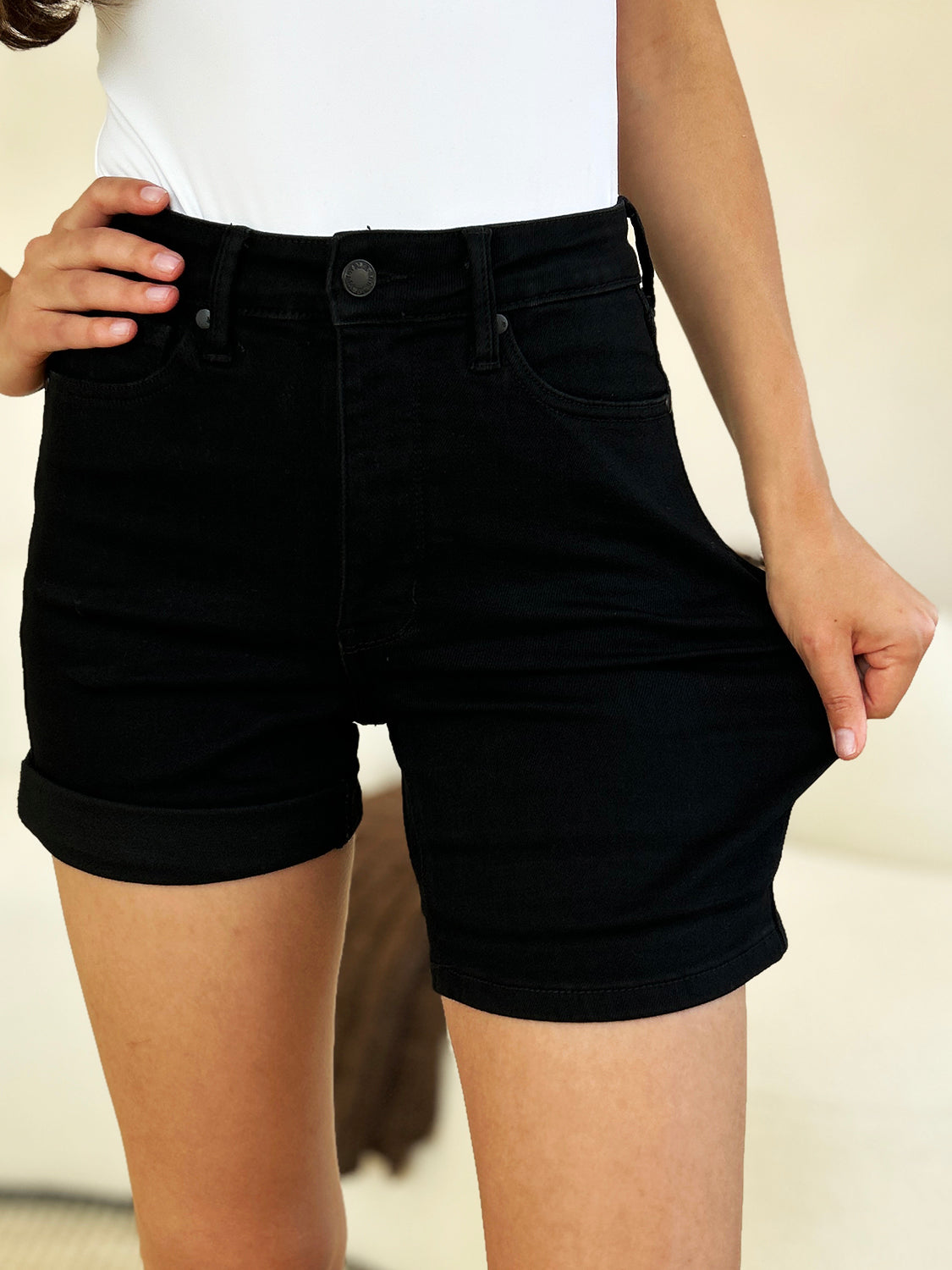 Person wearing a white top and Judy Blue Full Size High Waist Tummy Control Cuffed Denim Shorts, one hand in pocket.