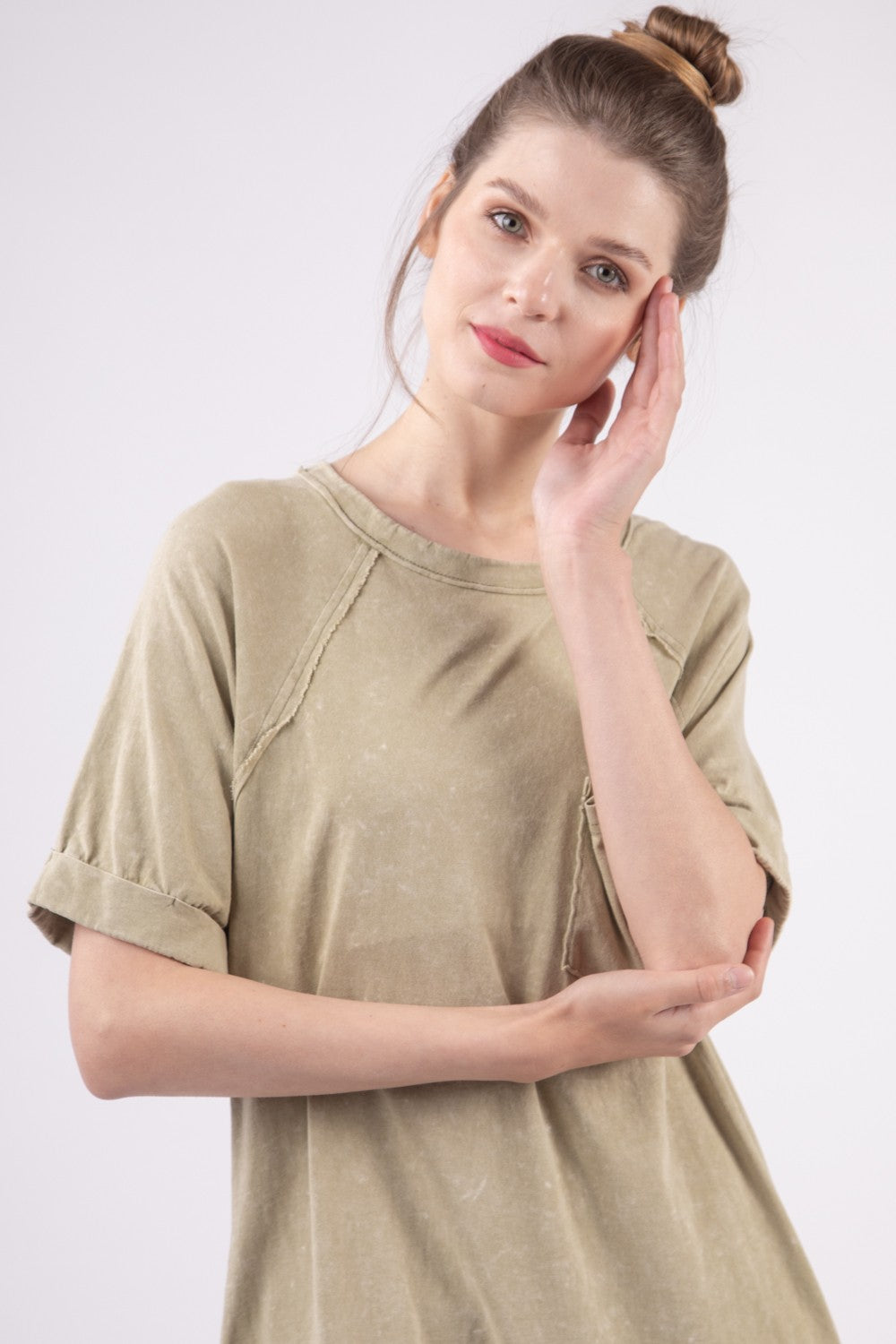 A woman in a VERY J Washed Round Neck Mini Tee Dress poses gracefully against a plain background. Her casual ensemble features an oversized beige tee dress complete with a pocket, radiating effortless style and comfort.