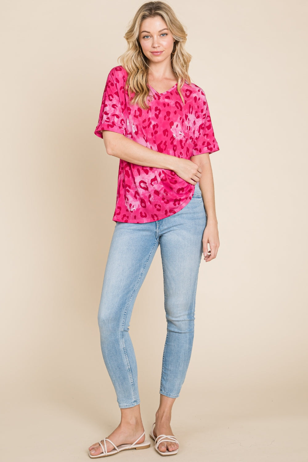 A person wearing the BOMBOM Leopard V-Neck Short Sleeve T-Shirt in a vibrant pink leopard print and light blue jeans poses against a beige background, smiling with one hand touching their hair.