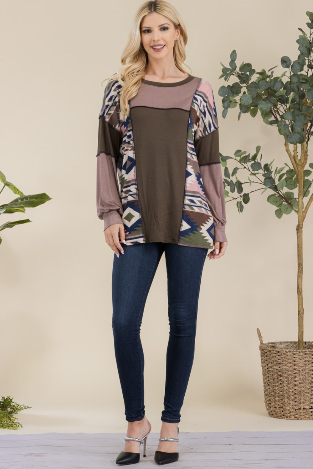 A woman with long blonde hair is wearing the Celeste Full Size Exposed Seam Printed Color Block T-Shirt and dark jeans, standing in front of a neutral background.