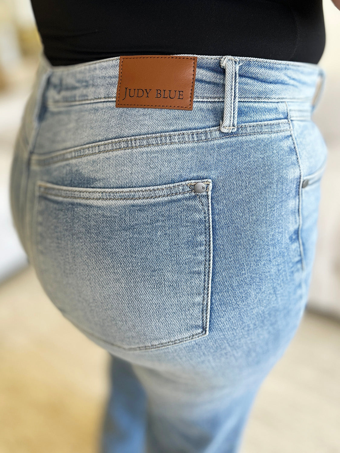 A person wearing Judy Blue Full Size High Waist Wide Leg Jeans and white shoes stands with hands in pockets. They are in front of a white couch and a green plant.