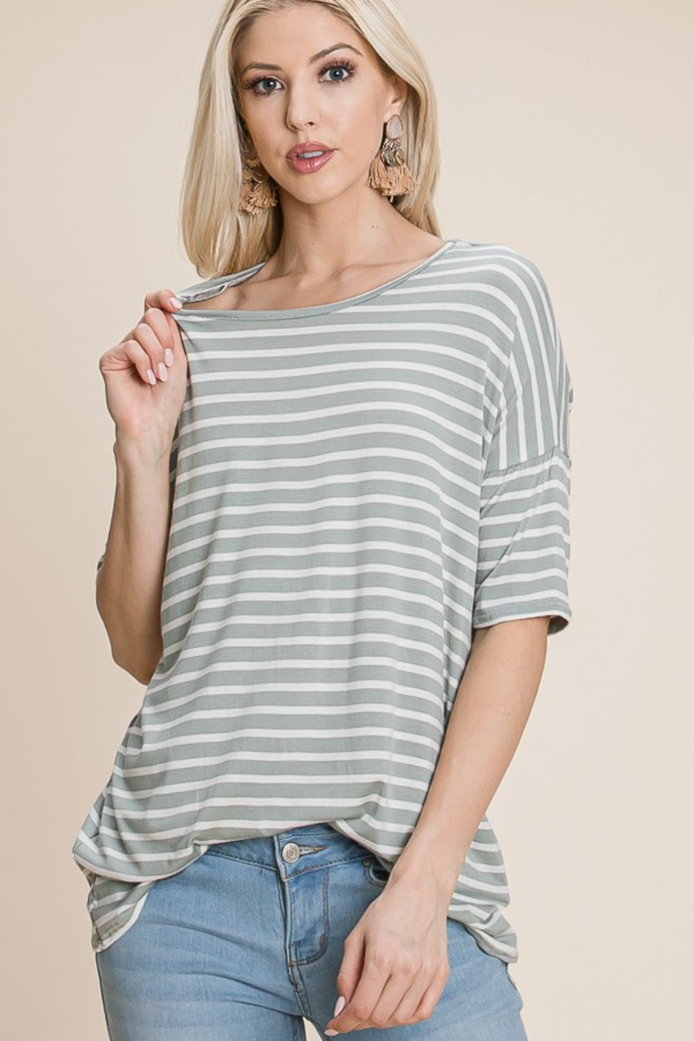 A woman with long blonde hair, dressed in a BOMBOM Striped Round Neck T-Shirt and blue jeans, exudes nautical charm while smiling and looking off to the side.