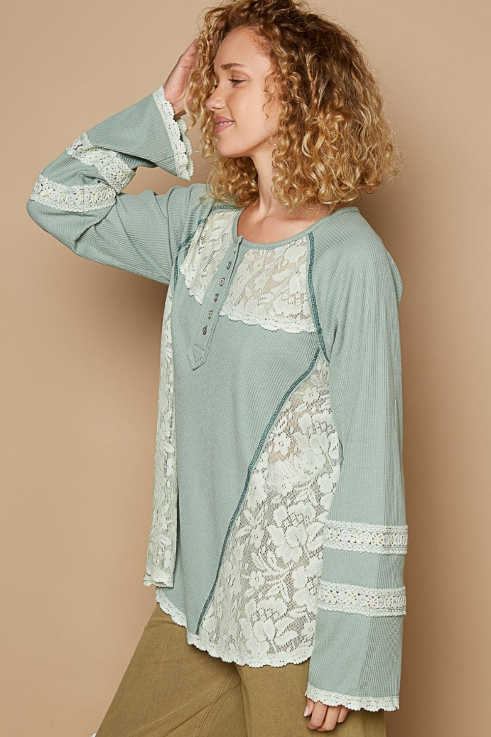 A woman with curly hair wears a pastel green POL Round Neck Long Sleeve Lace Trim Thermal Top with buttons on the front, standing against a plain beige background.