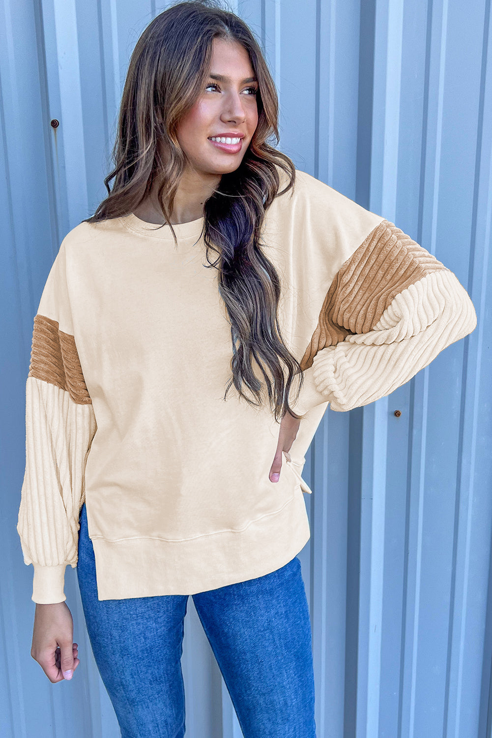 A person with long hair is wearing an Apricot Corduroy Patchwork Drop Shoulder Long Sleeve Sweatshirt, standing with their back to the camera against a light blue corrugated metal wall.