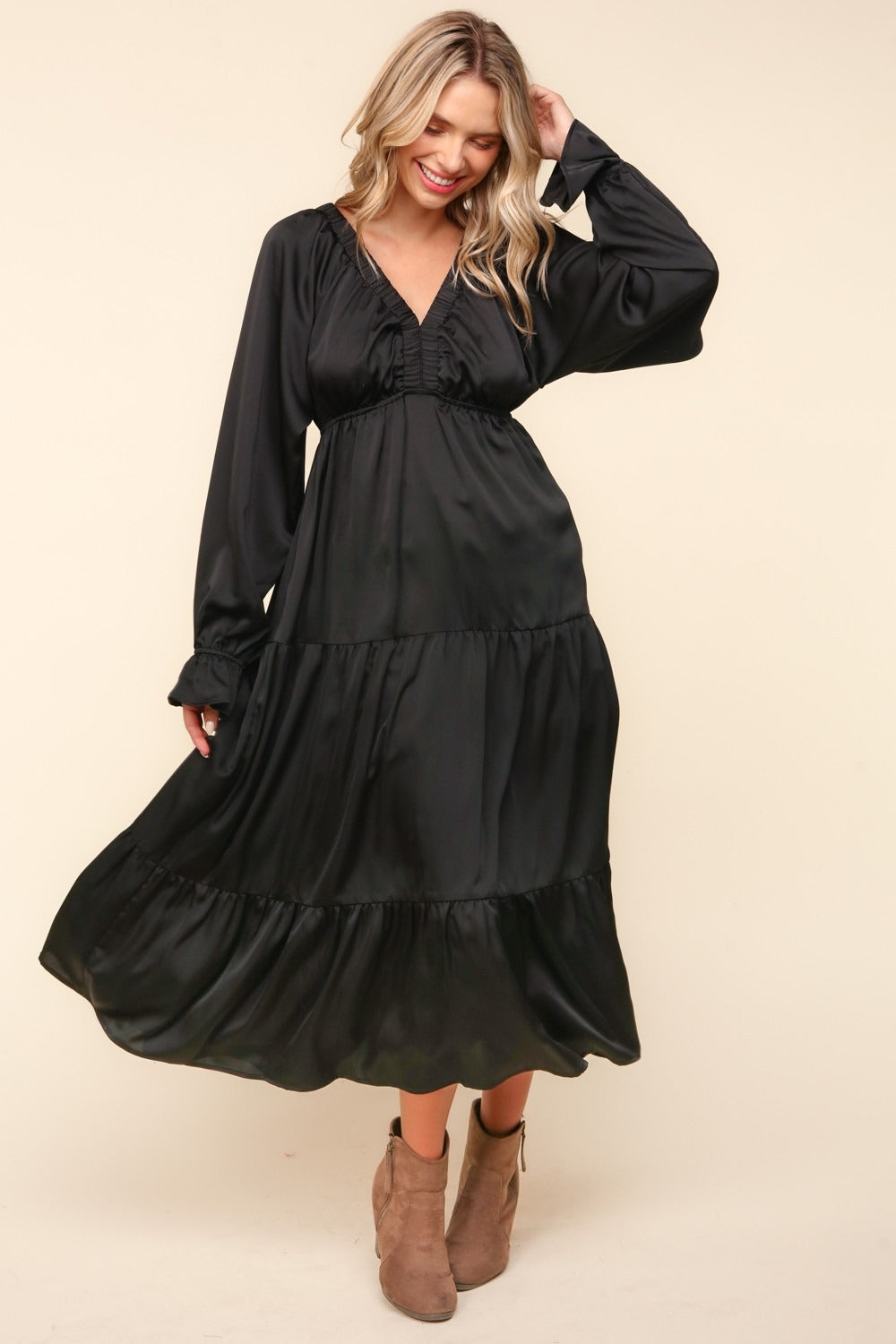 A woman stands wearing the Haptics Flounce Sleeve Tiered Midi Dress with Pockets in black, paired with brown ankle boots, against a plain background.