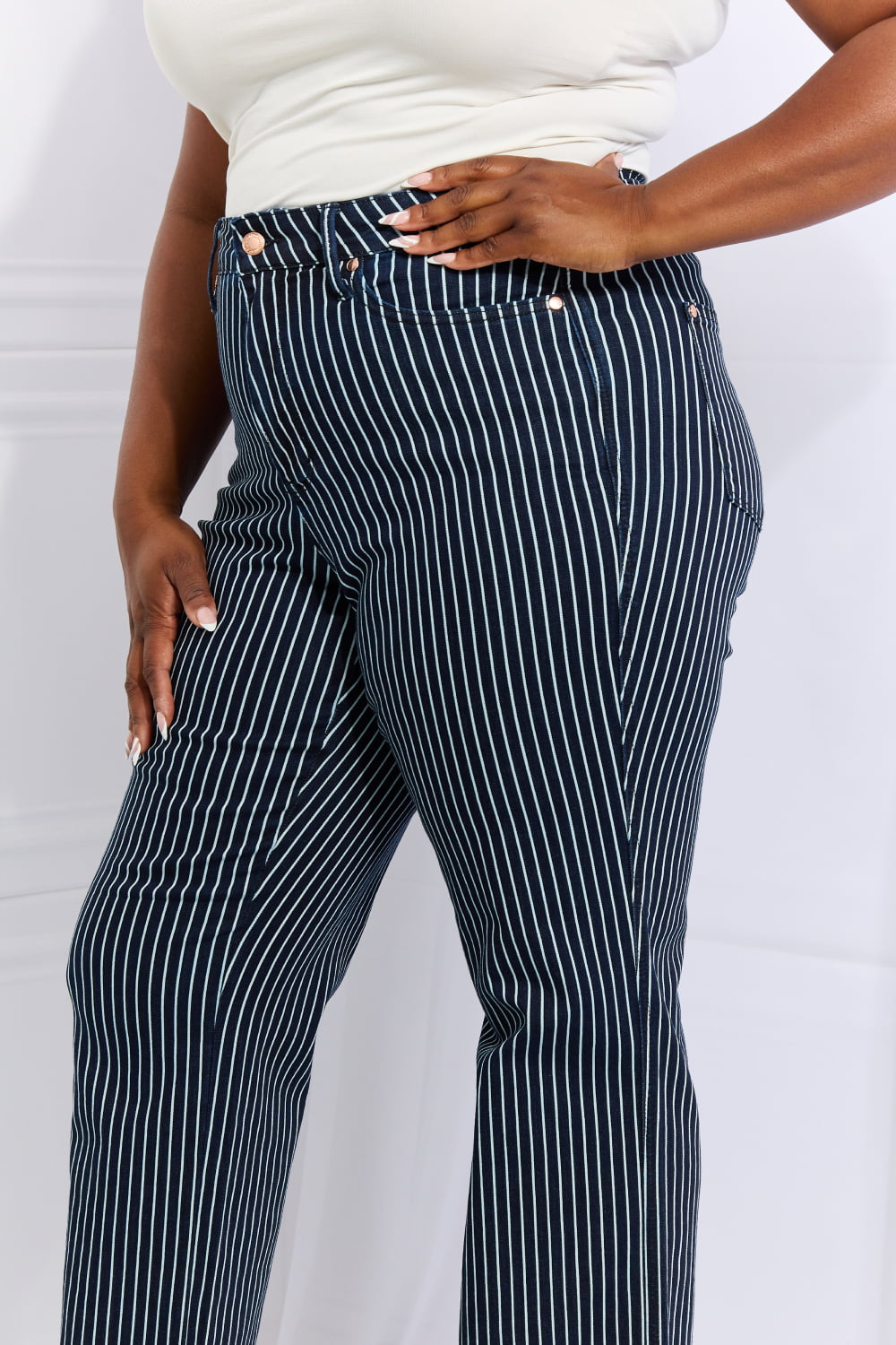 A person wearing Judy Blue Cassidy Full Size High Waisted Tummy Control Striped Straight Jeans, a white top, and tan platform sandals stands with one hand on their hip.