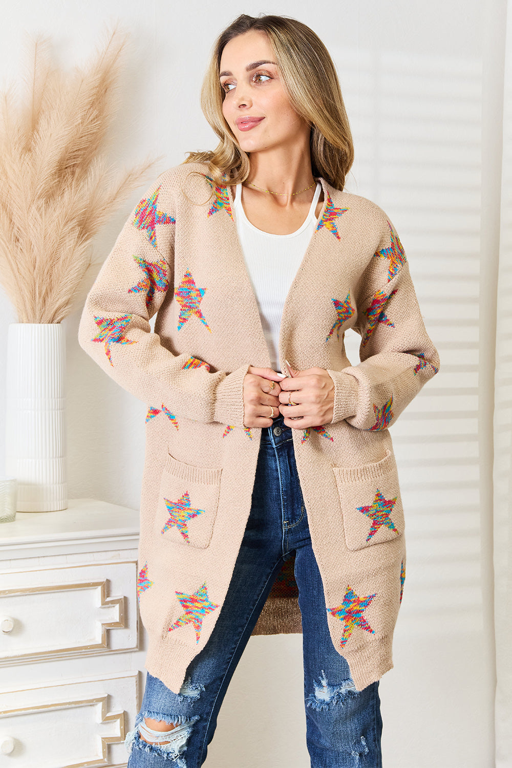 A woman stands indoors wearing the Angel Wings Star Pattern Open Front Longline Cardigan, pairing it with a white top and ripped jeans.