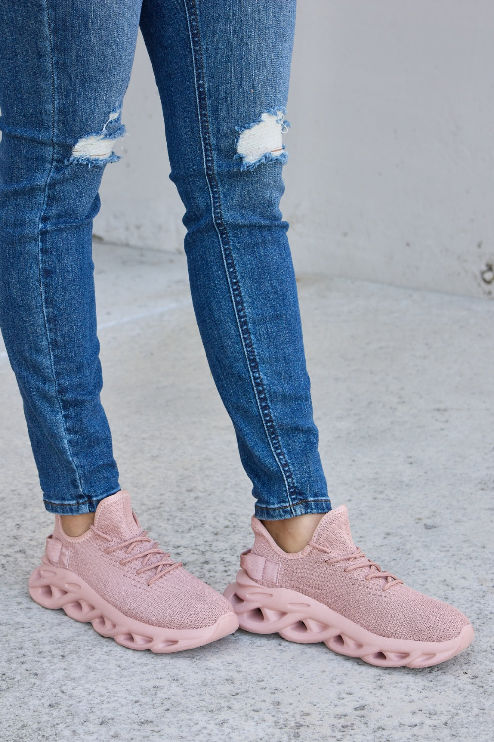 Person wearing blue ripped jeans and Forever Link Mesh Breathable Platform Athletic Shoes in light pink, standing on a concrete surface.