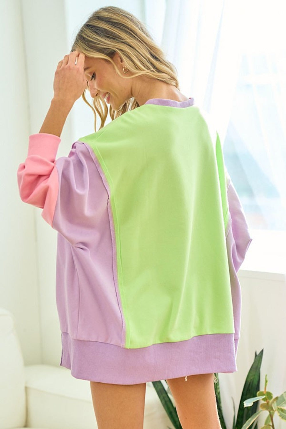 A woman wearing the First Love Color Block Long Sleeve Slit Sweatshirt and matching shorts poses indoors, smiling with one hand touching her hair.