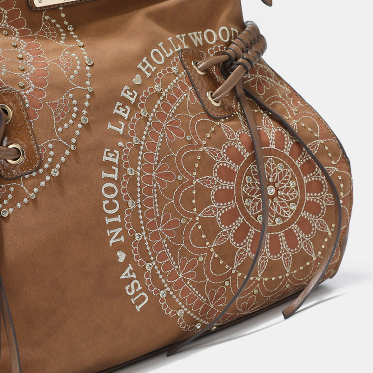 The Nicole Lee USA Side Braided Tassel Inlaid Rhinestone Embroidery Hobo Bag features intricately designed white mandala patterns on brown vegan leather, along with "Nicole Lee Hollywood USA" text. It includes top handles and decorative braided accents, as well as adjustable dual shoulder straps for added versatility.