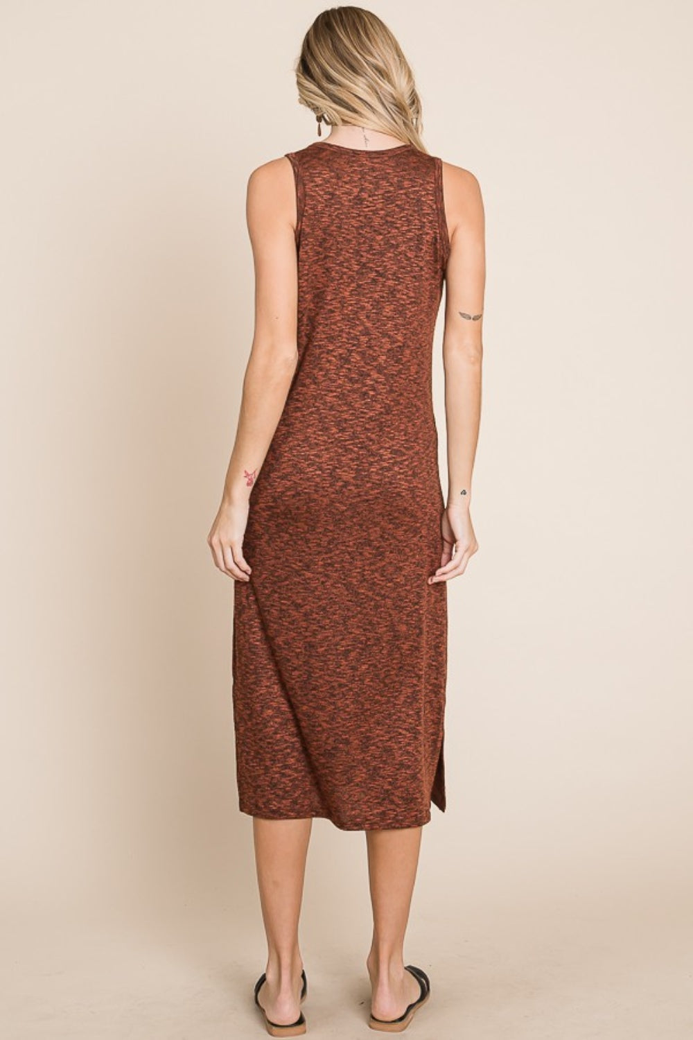 A woman with long blonde hair stands against a beige background, wearing the versatile and stylish BOMBOM Slit Round Neck Sleeveless Midi Dress in rust color, featuring a slit round neck and side slit, paired with black sandals.