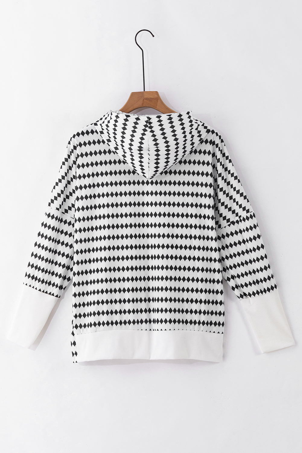 A woman in a Black Stripe Argyle Striped Half Button Oversized Hoodie stands in a room with light green brick walls, a painting of a sailboat, and a fan.