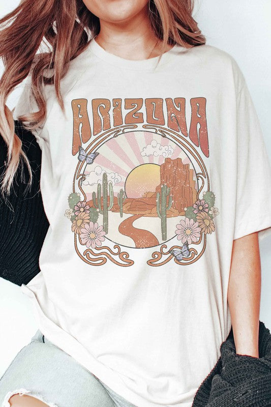 Someone wearing an ARIZONA DESERT Graphic Tee in unisex sizing, which showcases a lively desert scene with the word "Arizona," paired with light blue jeans. The tee's 100% cotton material enhances the comfort and style of this casual look.