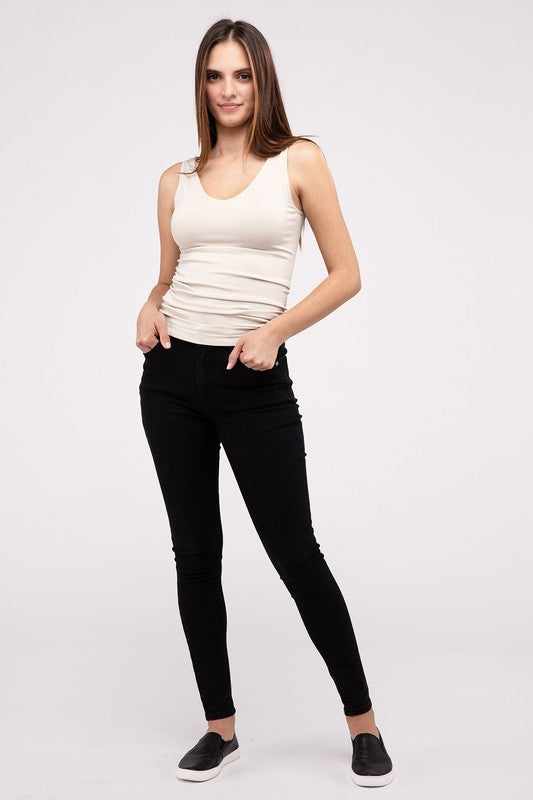 A woman in a white Front & Back 2-Way V-Neck Seamless Tank and black pants, standing with hands on hips and looking at the camera.