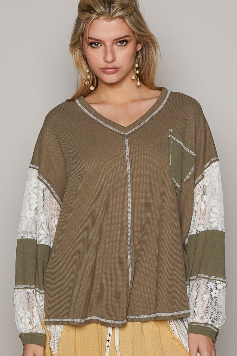 A person stands against a plain background, wearing a loose-fitting, patchwork outfit in shades of brown and beige. The ensemble features the POL V-Neck Lace Balloon Sleeve Exposed Seam Top paired with matching pants. They complete the look with black sandals.