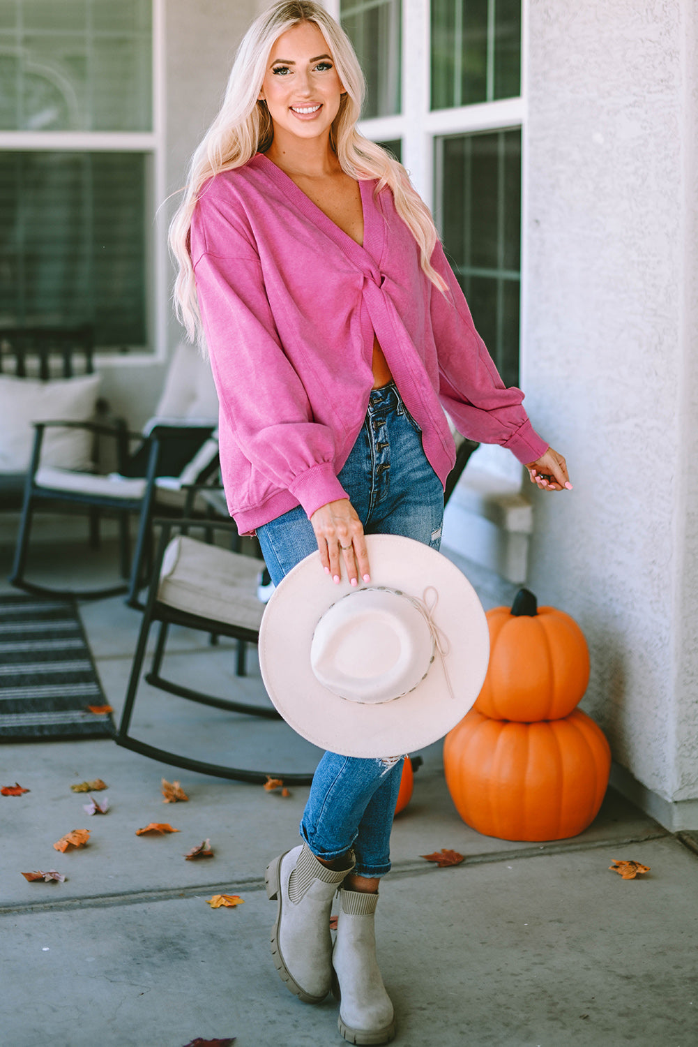 A woman stands with her back to the camera, wearing a long-sleeved Rose Exposed Seam Twist Open Back Oversized Sweatshirt and light blue jeans, showcasing a relaxed fit.