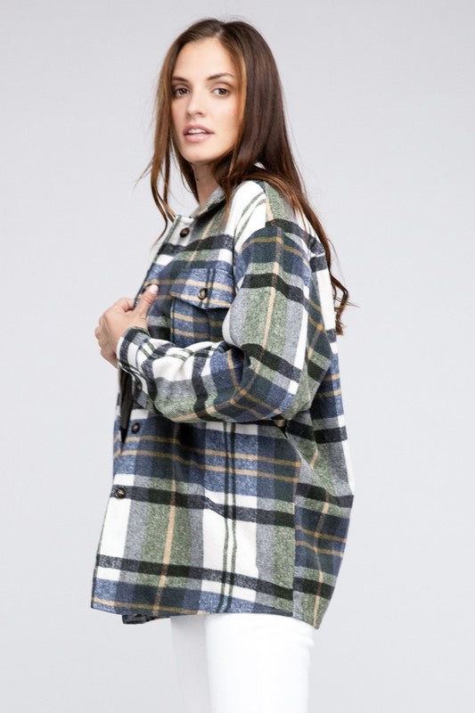 A woman in a Textured Shirt With Big Checkered Point leans casually against a wall, smiling while looking to the side. There are plants and a window in the background.