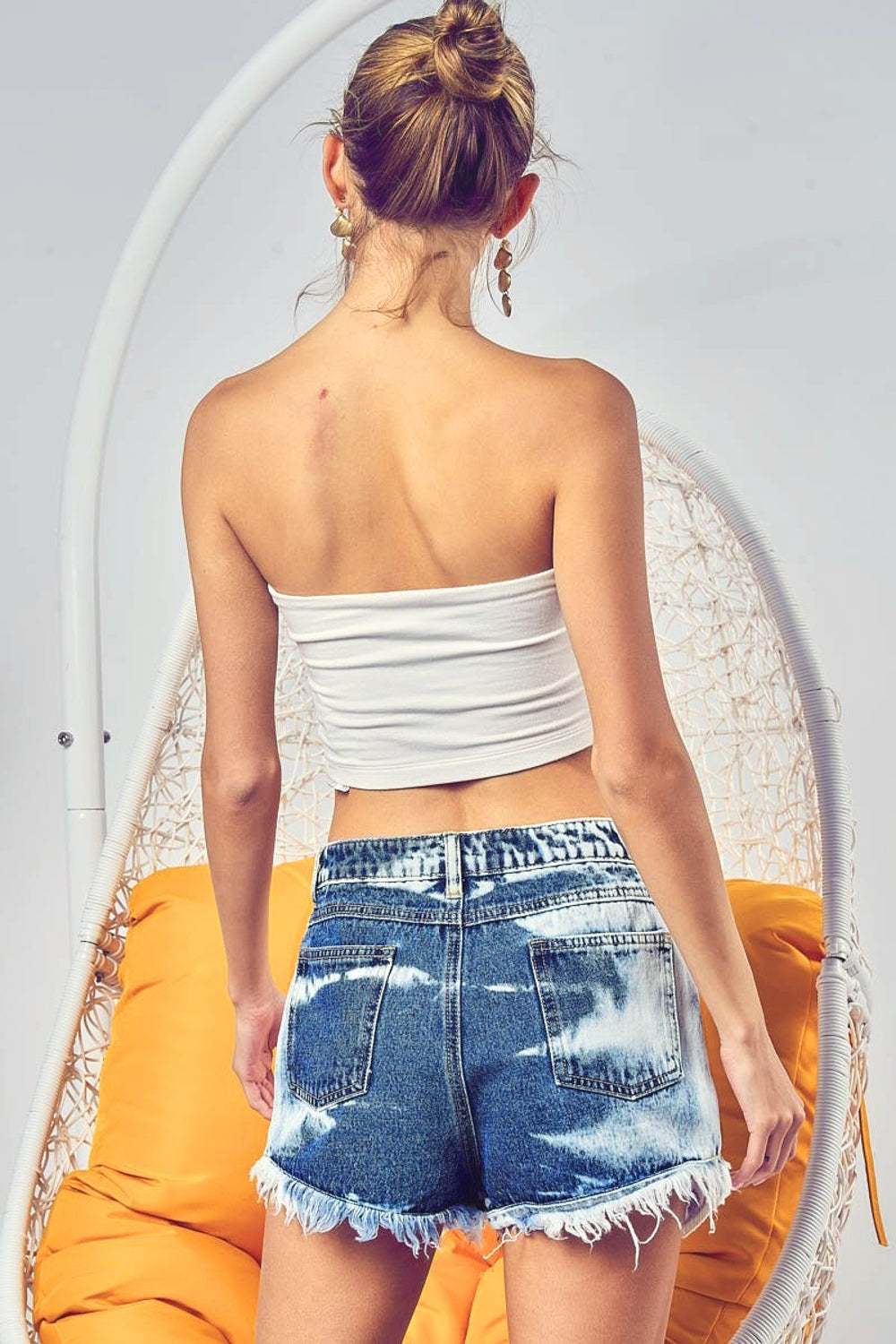 A person wearing BiBi US Flag Theme Bleached Denim Shorts and a white crop top stands with hands in pockets against a yellow background.