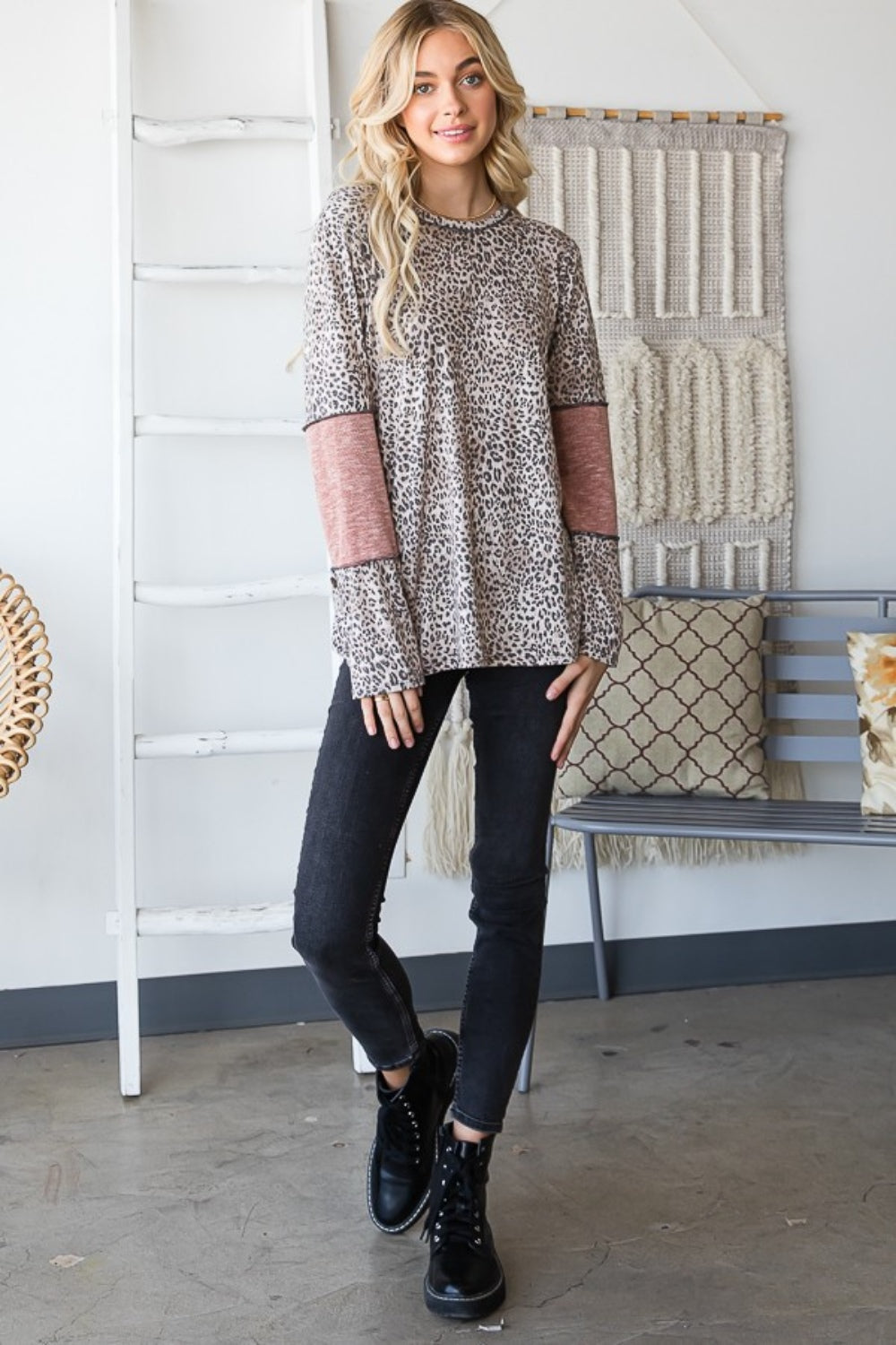 A fashion-forward individual in a Heimish Full Size Leopard Exposed Seam Contrast T-Shirt stands by a window, looking outside.