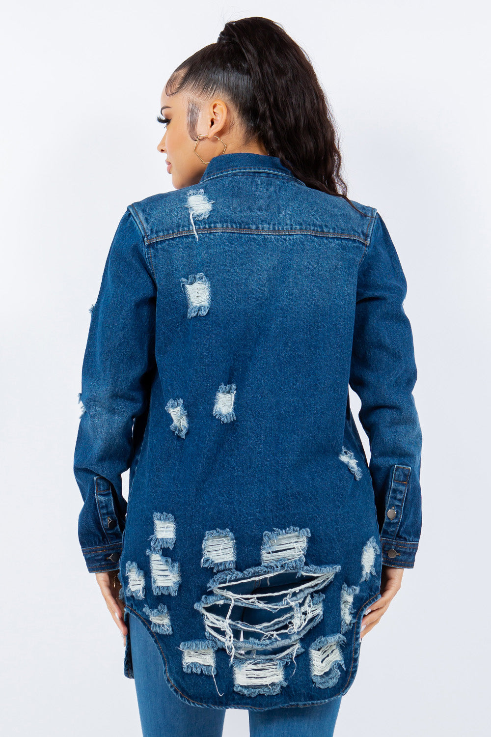 A woman is wearing an American Bazi Distressed Button Up Long Sleeve Denim Jacket over a white top and distressed jeans, posing against a plain background. The denim jacket adds an edgy touch to her chic ensemble.