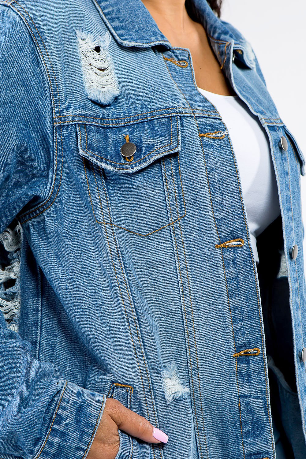 A woman in an American Bazi Full Size Button Up Distressed Denim Jacket with a vintage look stands against a plain background, pairing it perfectly with a white crop top and denim jeans.