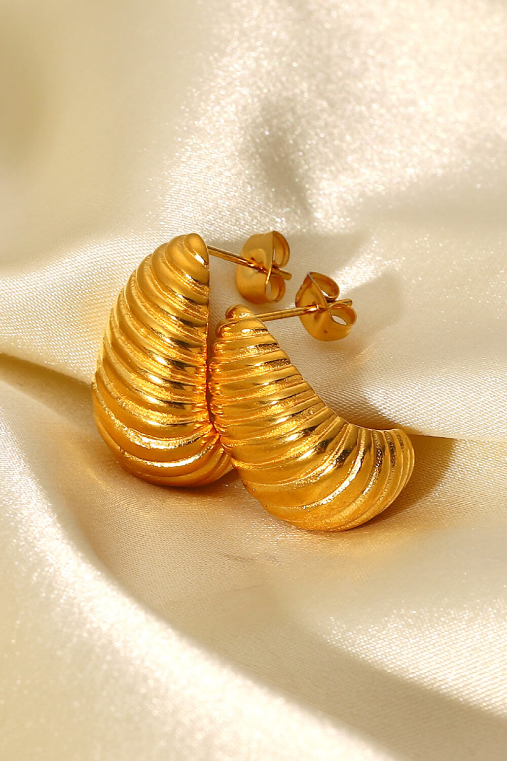 A pair of Shell Shore Spiral Stud Earrings, gold-plated with a ribbed, crescent shape and post-butterfly clasps on a white background.