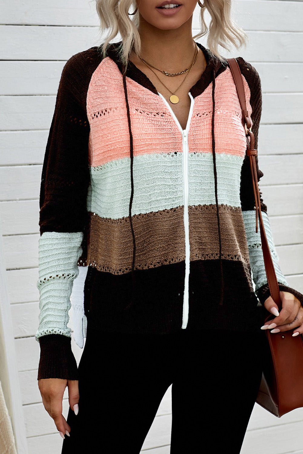 A person wearing the Brown Zipped Front Colorblock Hollow-out Knit Hoodie, featuring a multi-colored striped design with alternating bands of brown, pink, white, and gray. Seen from the back, the sweater showcases the hood and finely knitted texture. The person has long wavy hair—a perfect look for a bonfire on the beach.