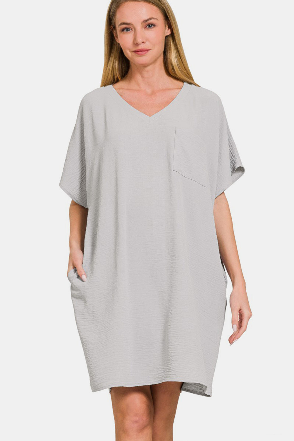 A person wearing the versatile light gray Zenana V-Neck Tee Dress with a chest pocket and a side pocket.