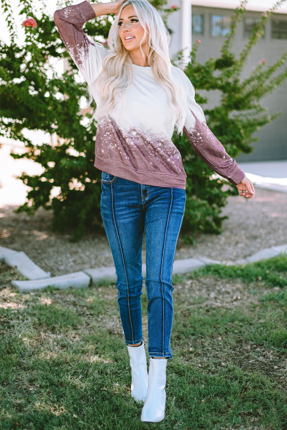 A person with long blonde hair is standing outdoors, facing away from the camera, wearing a Tie Dye Gradient Pullover Sweatshirt featuring a white and brown ombre splatter design.