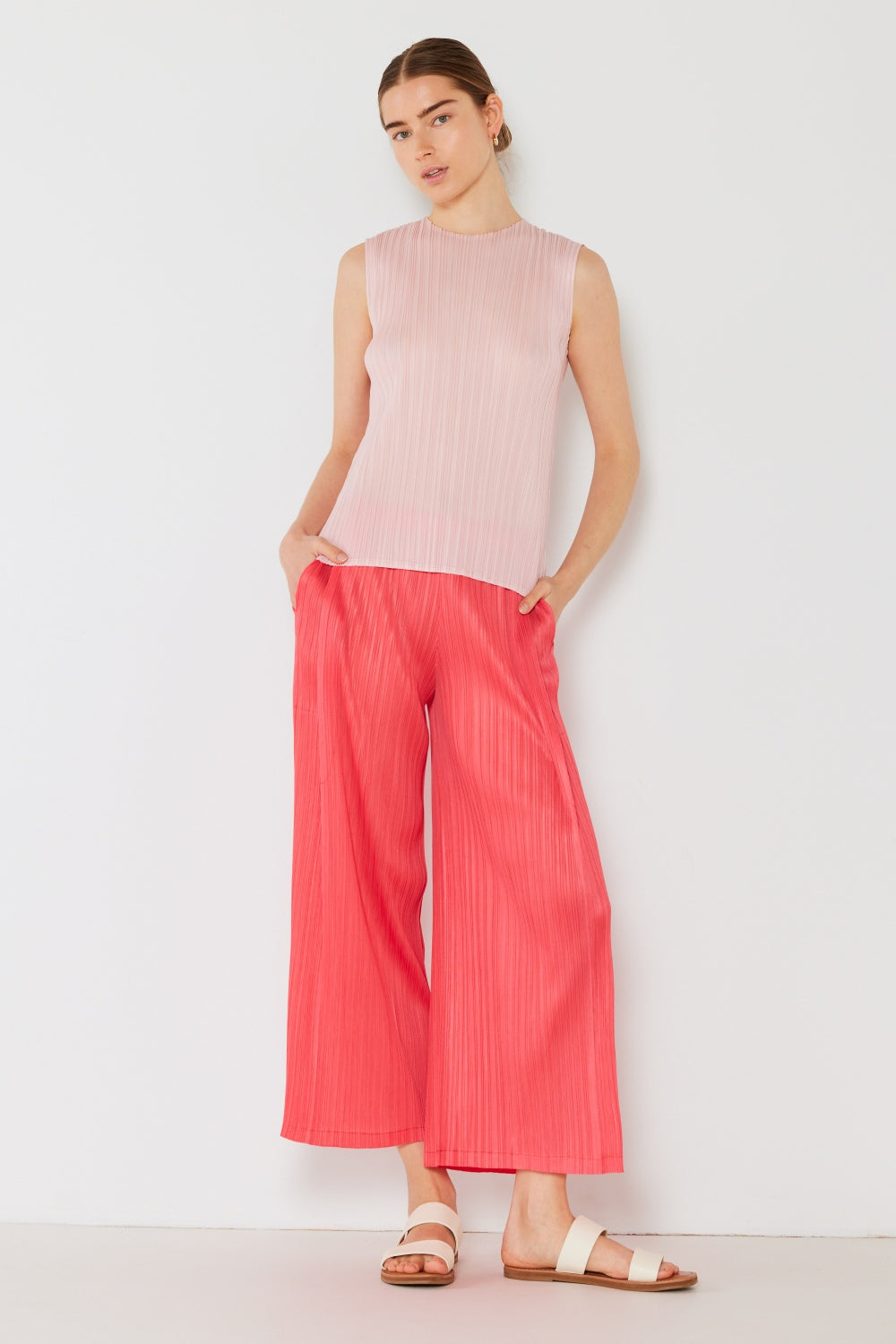 A person wearing the Marina West Swim Pleated Wide-Leg Pants with side pleat detail in red, standing against a white background with hands in pockets and wearing white sandals.