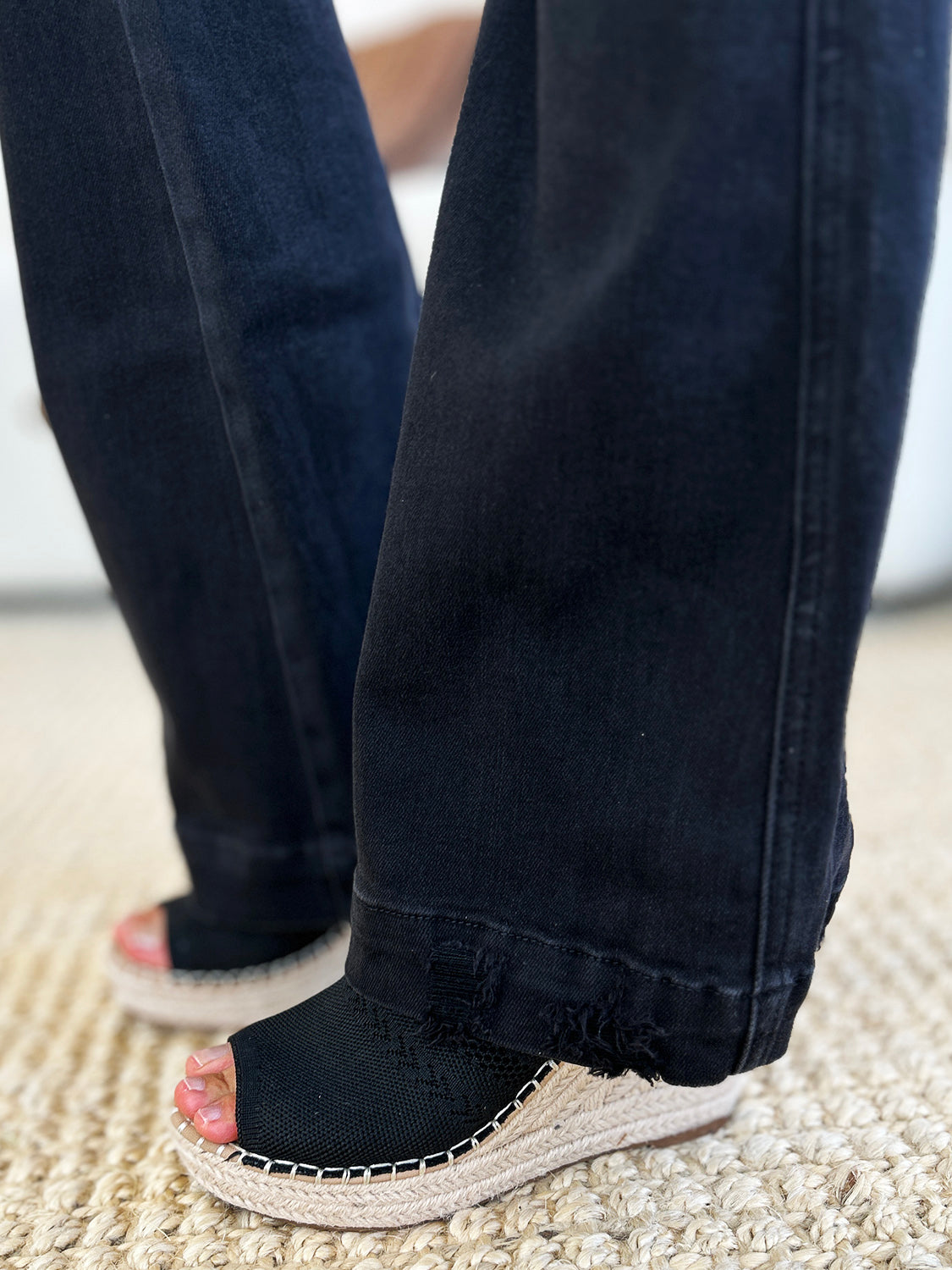 A person stands indoors, hands in pockets, wearing a white top and the Judy Blue Full Size High Waist Distressed Flare Jeans that create a flattering silhouette. In the background, a beige sofa and potted plants add to the retro-inspired look.