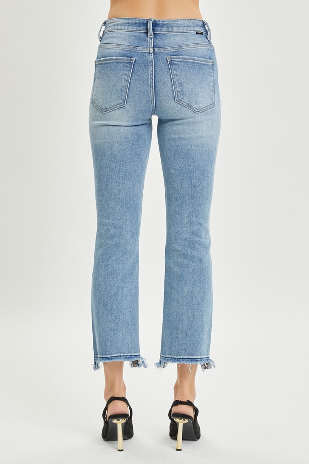 A person wearing the RISEN Full Size High Rise Distressed Cropped Straight Jeans in light blue with frayed hems, paired with black pointed-toe heels.