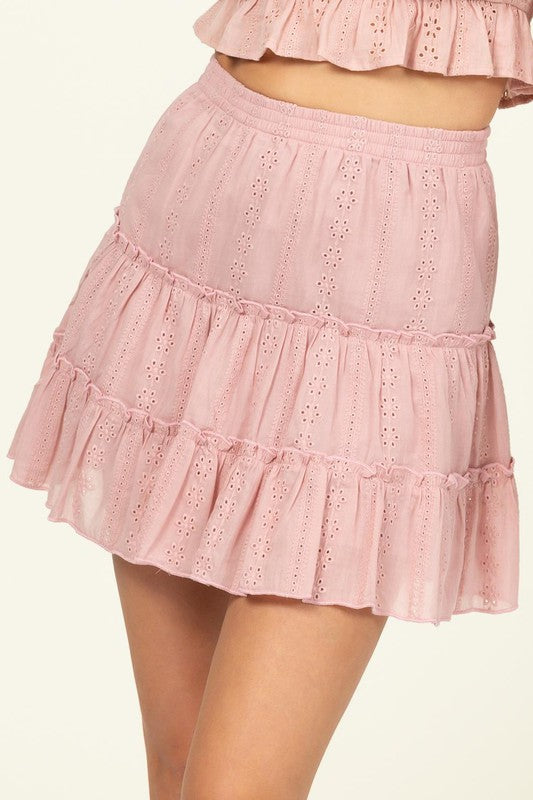 A person wearing the Forever Classy High Waist Tiered Mini Skirt in pink, featuring eyelet details and a ruffled design.