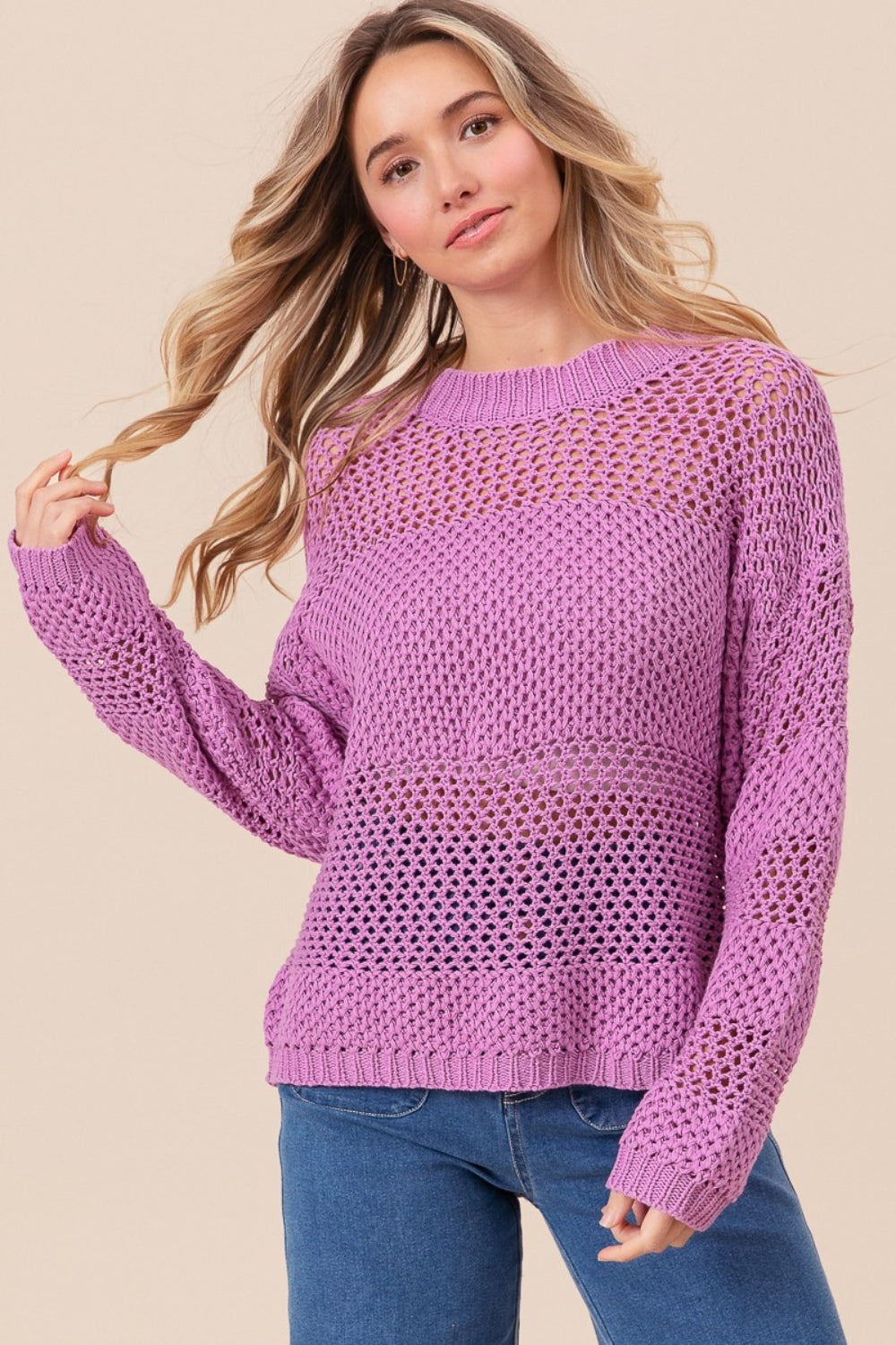 Wearing the BiBi Openwork Long Sleeve Knit Top in purple and blue jeans, a person smiles slightly while gazing to the side, exuding a fashion-forward vibe.