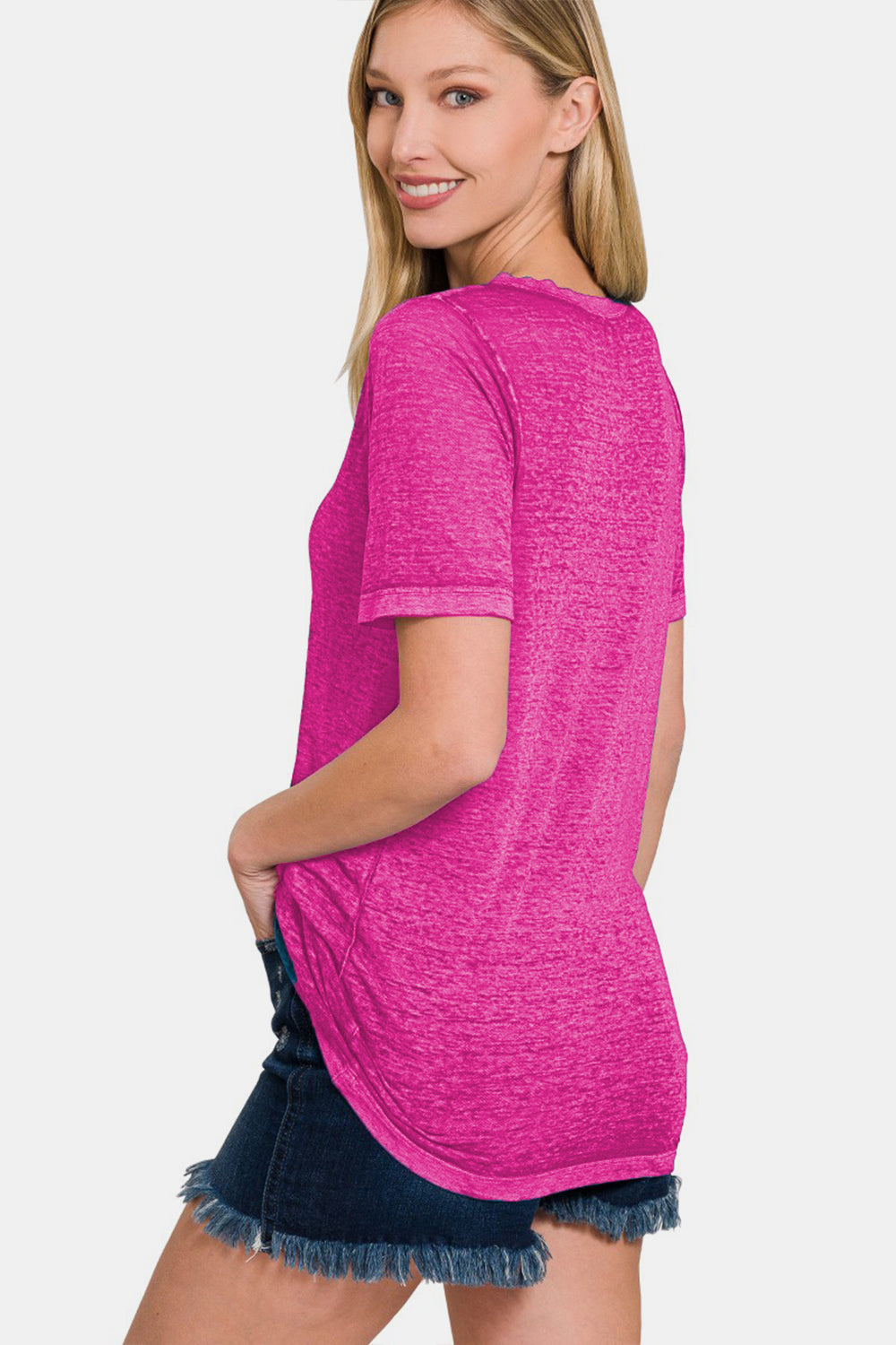 A woman is smiling and standing with her hand on her hip, wearing a pink Zenana V-Neck Short Sleeve T-Shirt made from comfortable fabric paired with denim shorts.