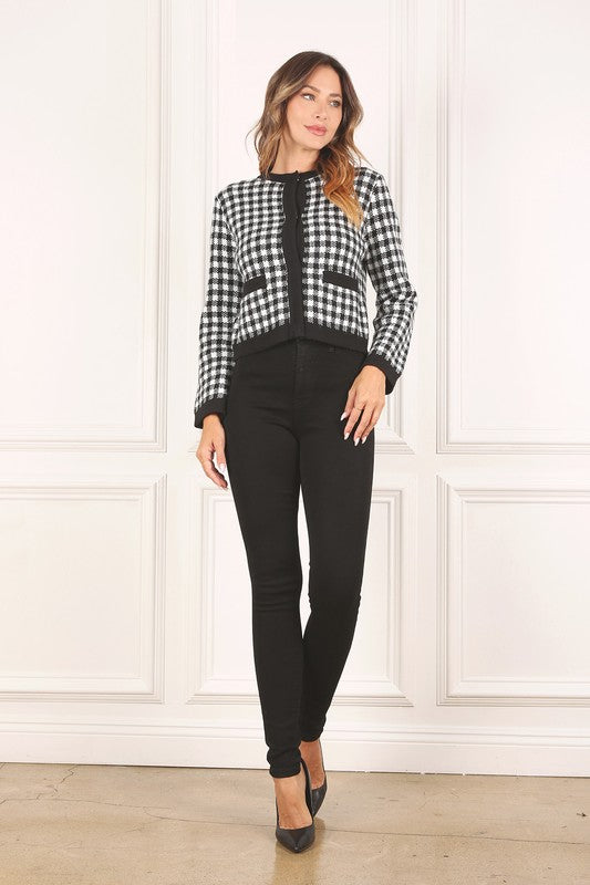 A woman dressed in the Black Check Knitted Jacket, featuring snap buttons and functional pockets, complemented by black pants, stands against a white background.