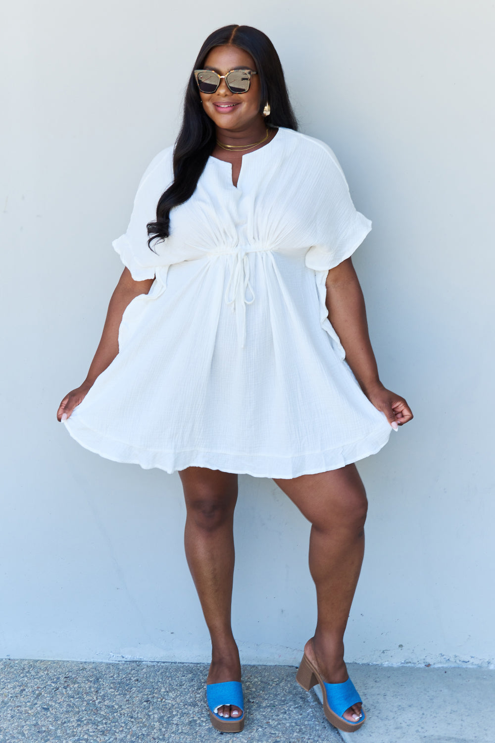 A person with long dark hair smiles while posing in the Ninexis Out Of Time Full Size Ruffle Hem Dress with Drawstring Waistband in White against a plain background.