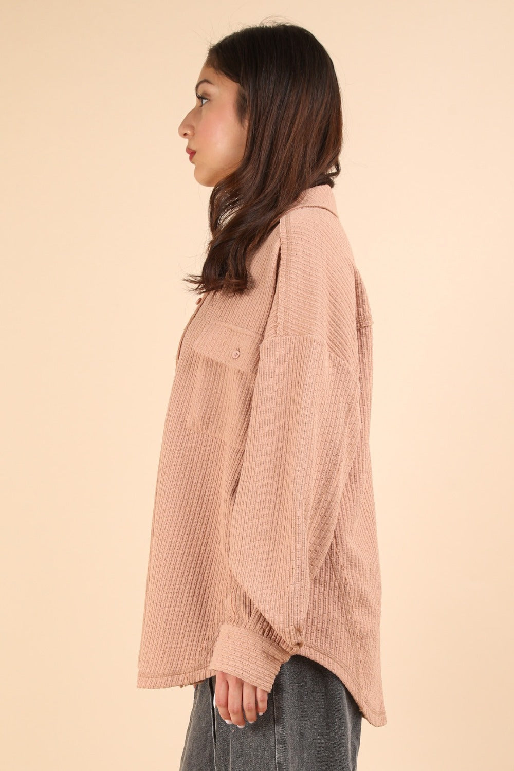 A woman wearing the VERY J Button Down Textured Knit Shacket in an oversized beige style over a black top stands against a plain background, showcasing the perfect transitional piece for any wardrobe.