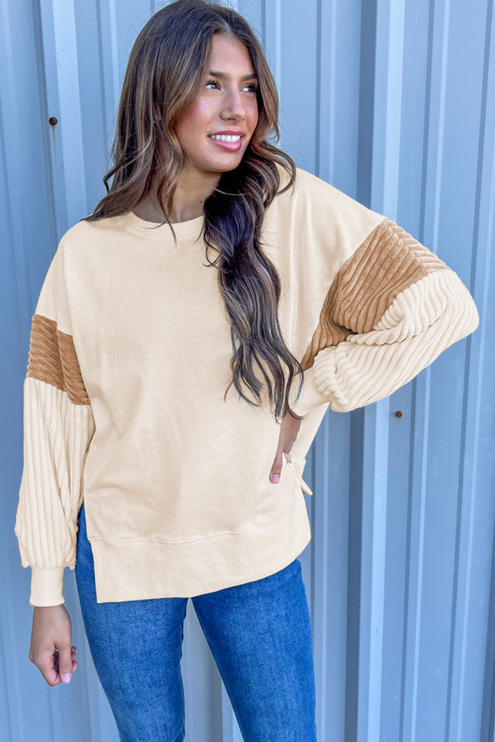 A person with long hair is wearing an Apricot Corduroy Patchwork Drop Shoulder Long Sleeve Sweatshirt, standing with their back to the camera against a light blue corrugated metal wall.