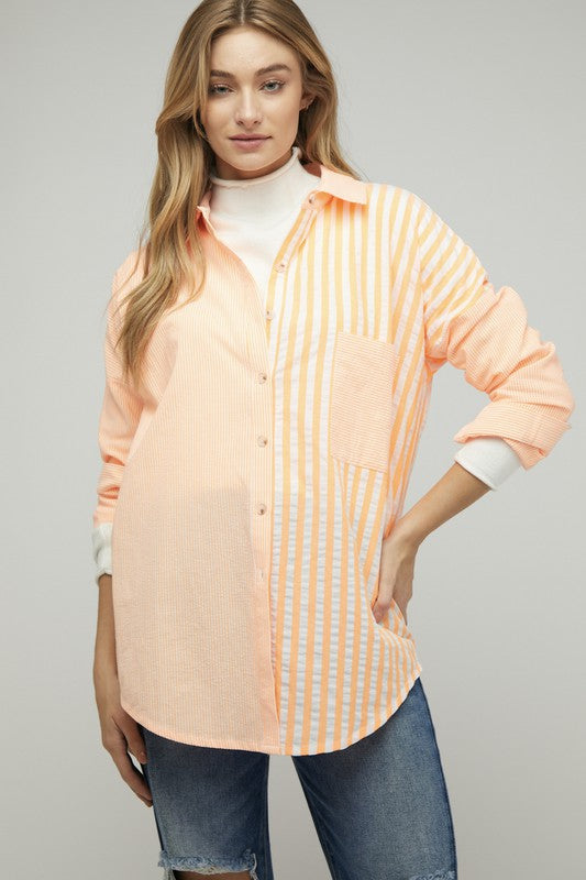 A person wearing a light pink Stripe Button Down Long Sleeve Shirt with rolled-up sleeves and jeans stands with their hands behind their head against a plain background.