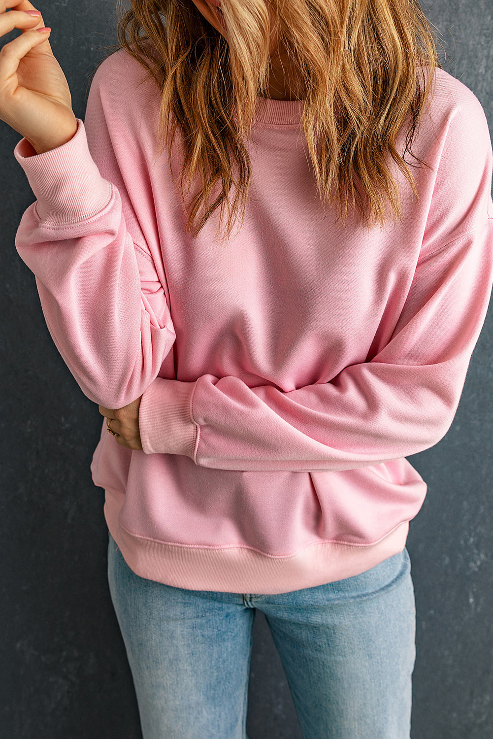 Individual with wavy brown hair wearing a Pink Plain Crew Neck Pullover Sweatshirt and blue jeans, standing with their back to the camera.