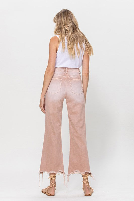 Person wearing 90's Vintage Crop Flare Jeans in rose pink with high waist, distressed details, rips on the knees, and frayed hems, paired with beige strappy sandals.