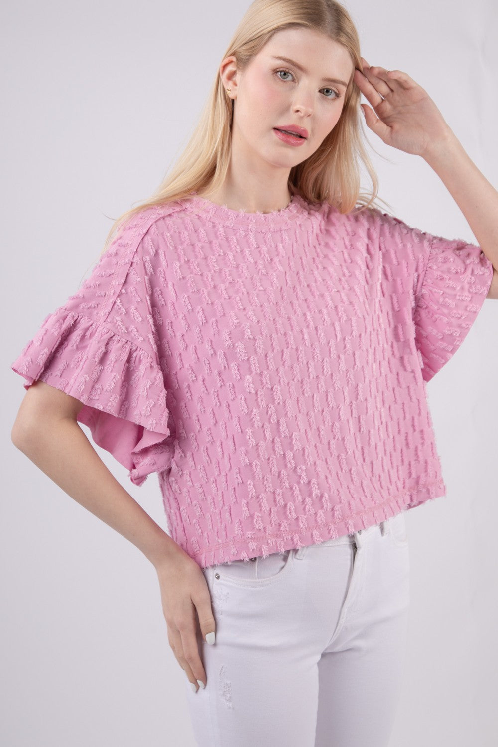 Person wearing the VERY J Full Size Texture Ruffle Short Sleeve Top, a chic and feminine textured pink blouse, paired with white pants, standing against a plain background.