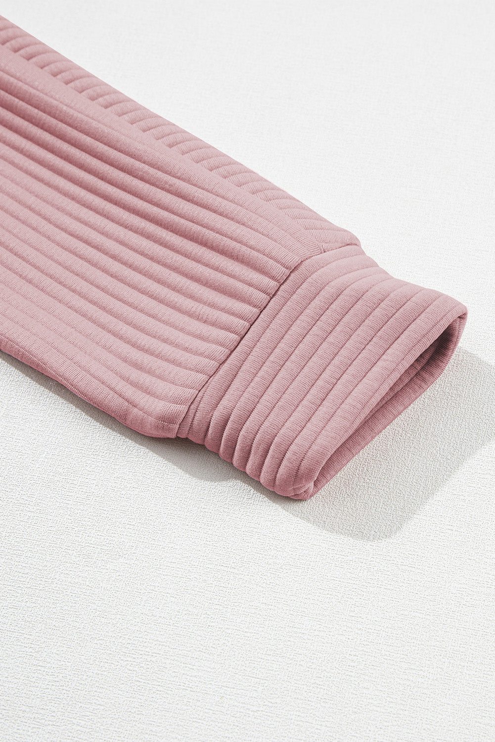 A person wearing a Peach Blossom Ribbed Texture Quarter Zip Sweatshirt and light blue jeans is standing with their back to the camera, holding a beige clutch.