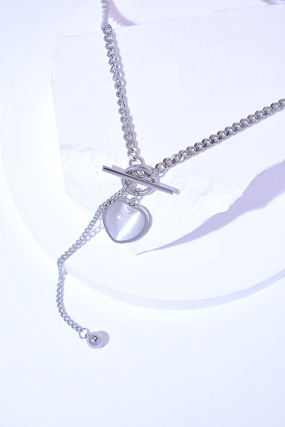 A Titanium Steel Heart Necklace with a heart-shaped pendant and a small key charm, featuring a delicate cat's eye stone, on a white background.