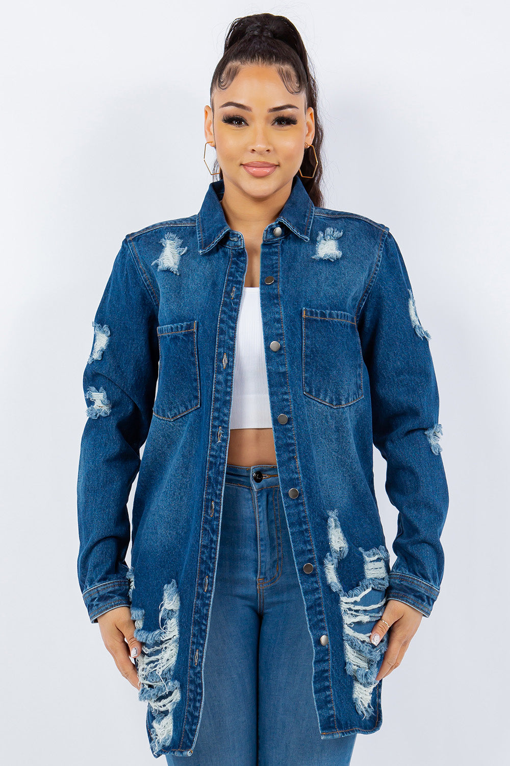 A woman is wearing an American Bazi Distressed Button Up Long Sleeve Denim Jacket over a white top and distressed jeans, posing against a plain background. The denim jacket adds an edgy touch to her chic ensemble.