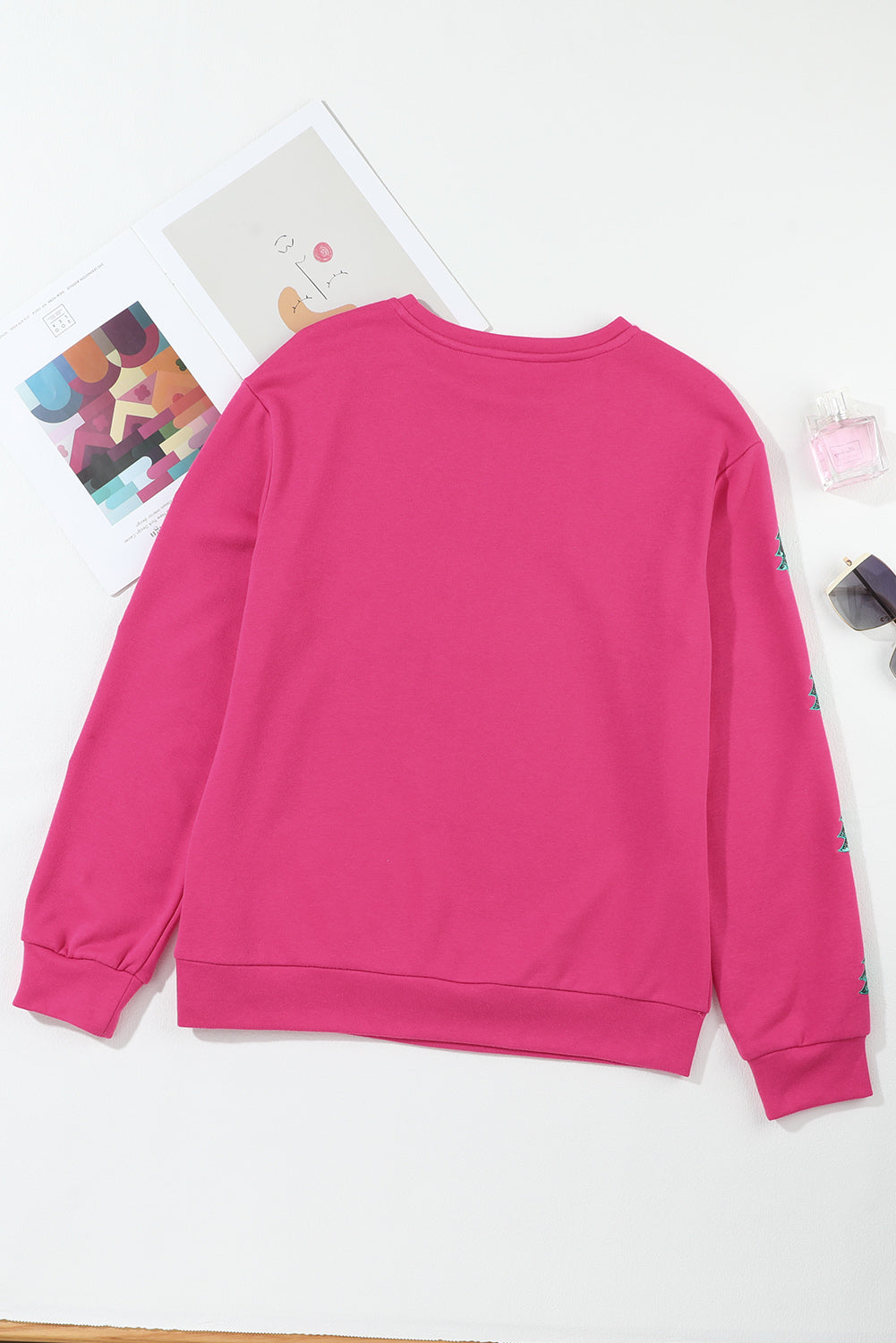 A person with wavy hair is standing with one hand on their hip, wearing a Strawberry Pink MERRY Christmas Tree Sequin Patchwork Sweatshirt and blue jeans. The person is facing away from the camera.