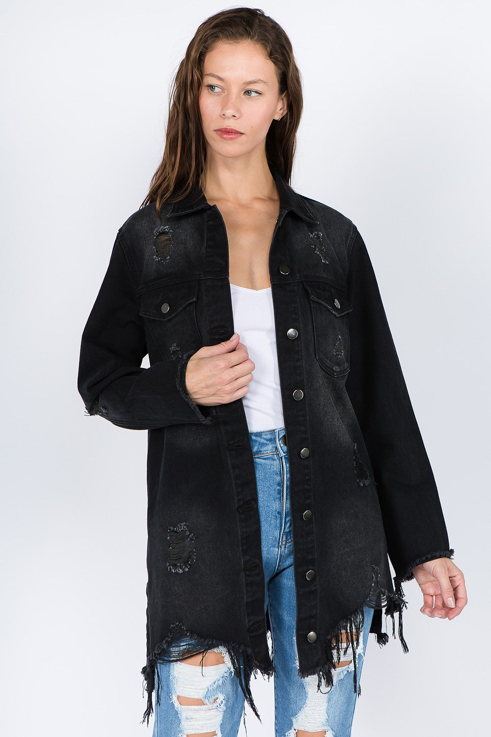 A woman wearing the American Bazi Distressed Frayed Hem Denim Jacket over a white top and ripped blue jeans stands against a plain background, giving her outfit a vintage feel.